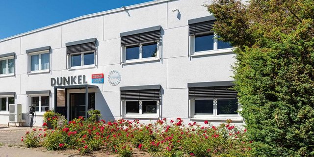 Das Gebäude mit dem Schriftzug 'DUNKEL' hat eine moderne Fassade und ist von bunten Rosen umgeben.