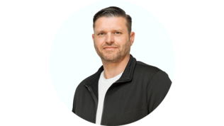 Ein Mann mit kurzem, gestyltem Haar und Bart lächelt freundlich in die Kamera, gekleidet in einen schwarzen Reißverschluss-Pullover.