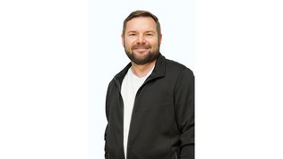 Der Mann mit einem freundlichen Lächeln steht in einer schwarzen Jacke und strahlt Selbstbewusstsein aus.