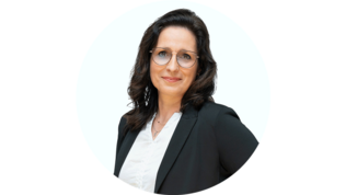 Die Frau hat eine positive Ausstrahlung, trägt eine weiße Bluse und posiert vor einem hellen, runden Hintergrund.