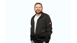 Der Mann steht entspannt mit verschränkten Armen da, sein lächelndes Gesicht strahlt Selbstbewusstsein aus.