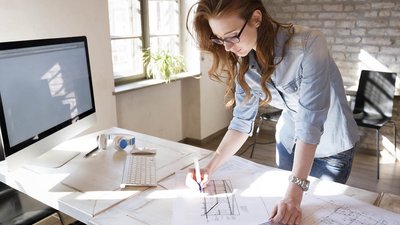 Eine Frau steht an einem Bürotisch und makiert eine Technische Zeichnung